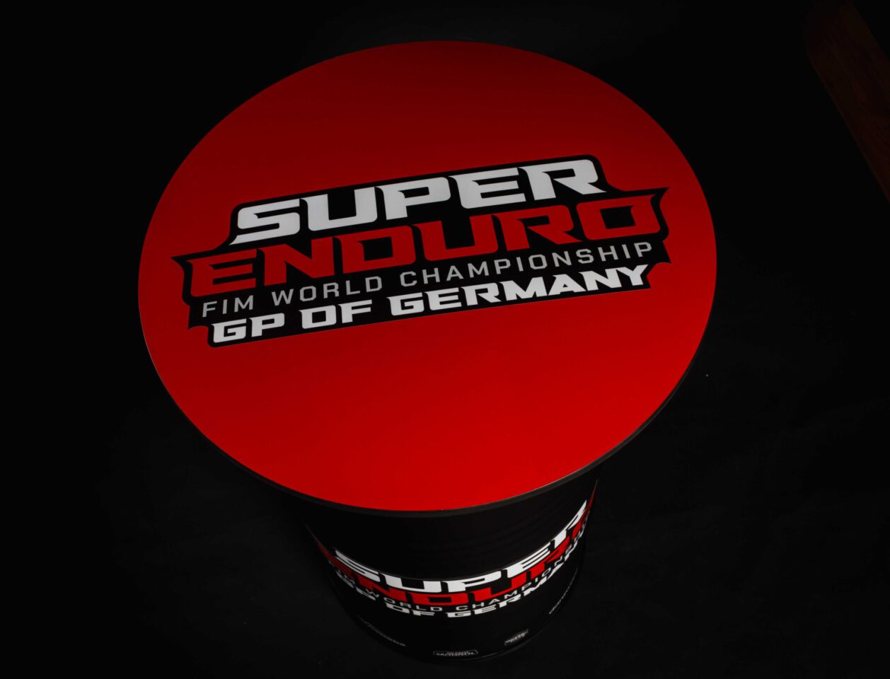 Schwarz-mattes Superenduro Stehfass von der Fasswerkstatt mit roter Tischplatte und der Aufschrift "Super Enduro FIM World Champions GP OF GERMANY"