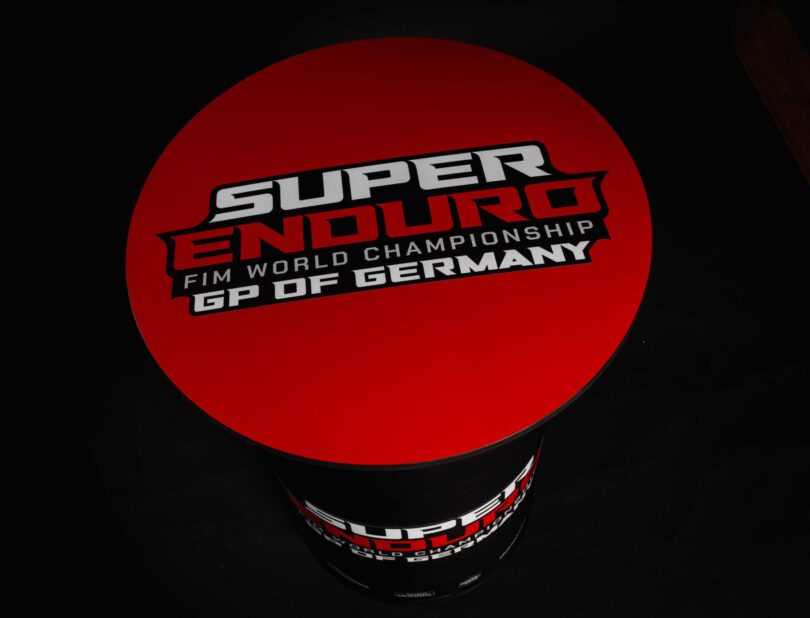 Schwarz-mattes Superenduro Stehfass von der Fasswerkstatt mit roter Tischplatte und der Aufschrift "Super Enduro FIM World Champions GP OF GERMANY"