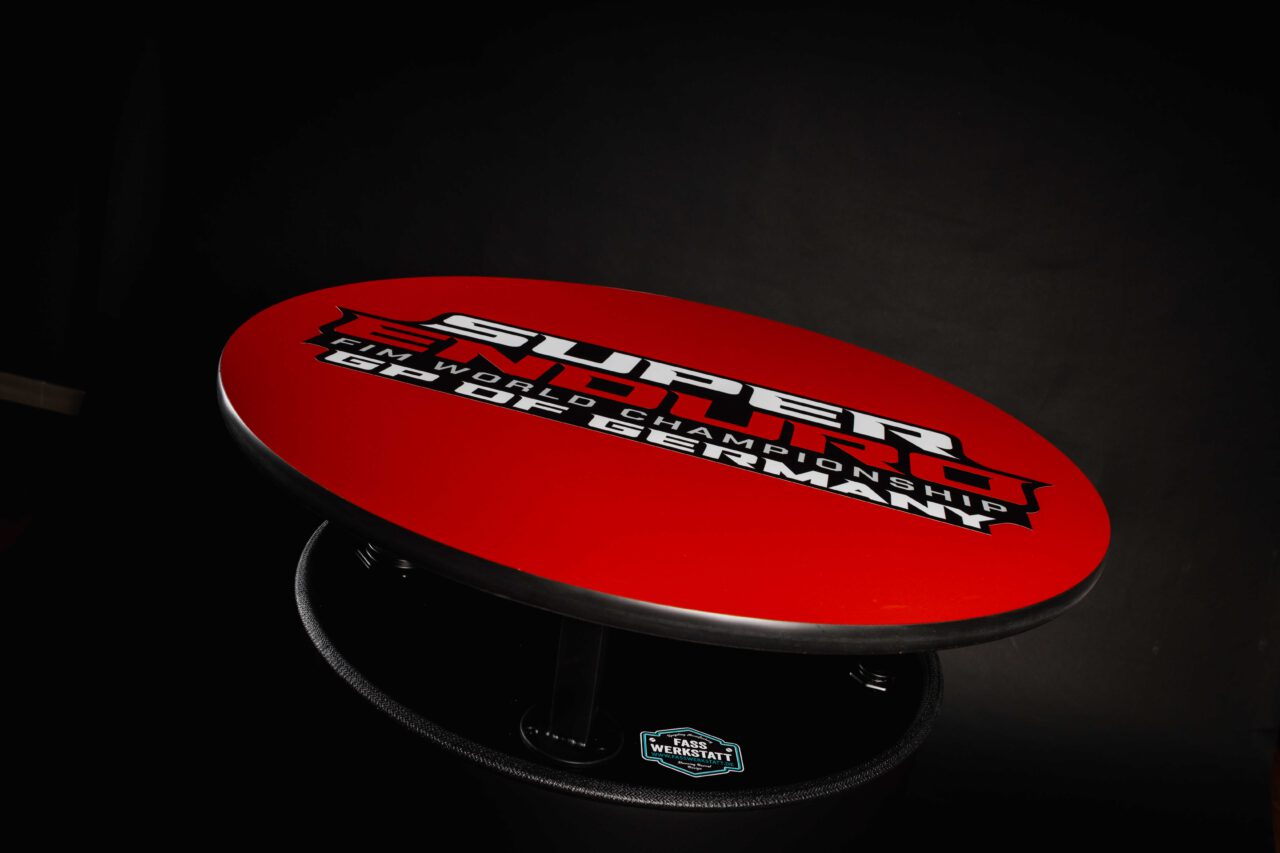 Schwarz-mattes Superenduro Stehfass von der Fasswerkstatt mit roter Tischplatte und der Aufschrift "Super Enduro FIM World Champions GP OF GERMANY"