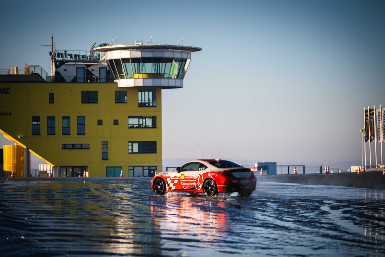 Roter Sachsenring Sportwagen von weit weg, im Hintergrund Start-und Zielturm Sachsenring.
