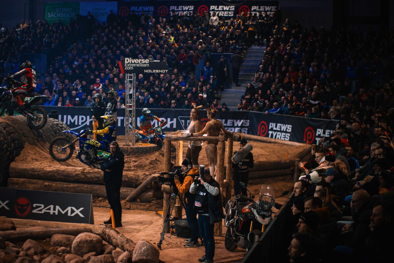 Motocross-Fahrer springt mit Motorrad über Hindernis aus großen Reifen vor vollbesetzter Tribüne in Halle.