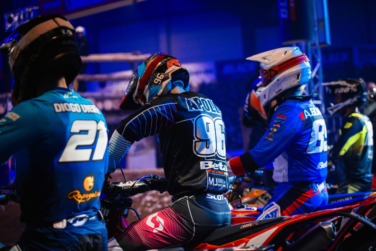 Drei Motorradfahrer in Rennkleidung und Helmen sitzen auf ihren Motorrädern, die Startnummern 21, 96 und 83 tragen.