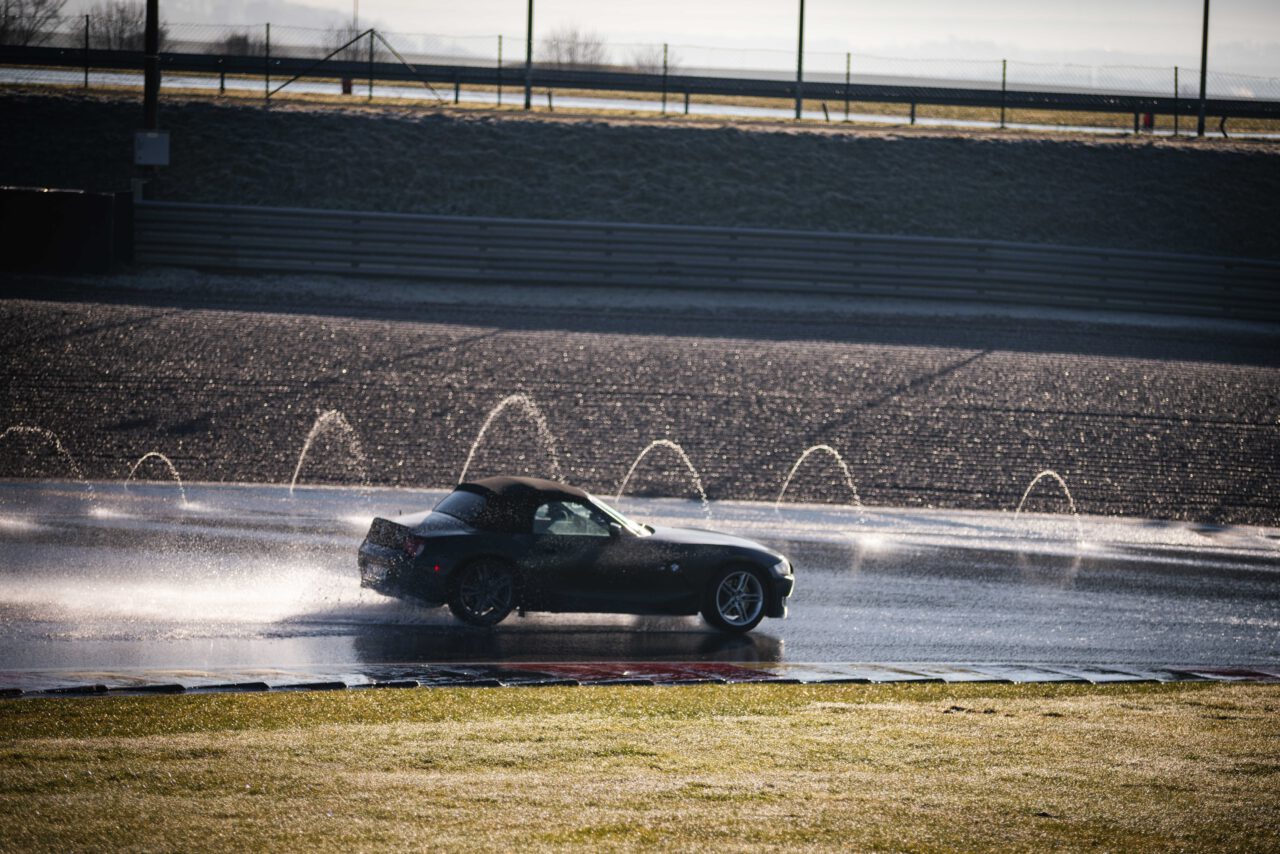 Schwarzes, kleines, schickes Auto, welches auf präparierter nasser Fahrbahn fährt.