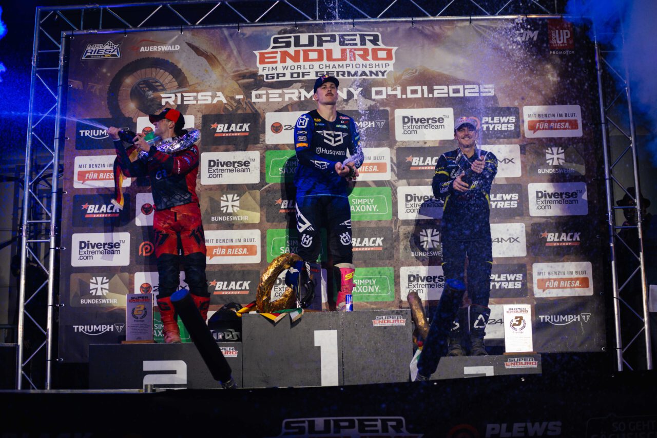 Drei Motorradrennfahrer auf dem Siegerpodest bei der Super Enduro FIM World Championship in Riesa, Deutschland, am 4. Januar 2023, umgeben von Sponsorentafeln.