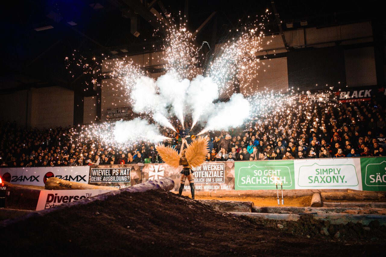 Person mit Flügeln steht vor Zuschauermenge, Feuerwerkskörper explodieren in hellem Funkenregen