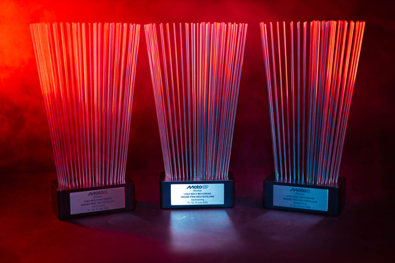 Drei Auszeichnungen mit vielen dünnen Metallstäben auf schwarzen Sockeln vor rotem Hintergrund.