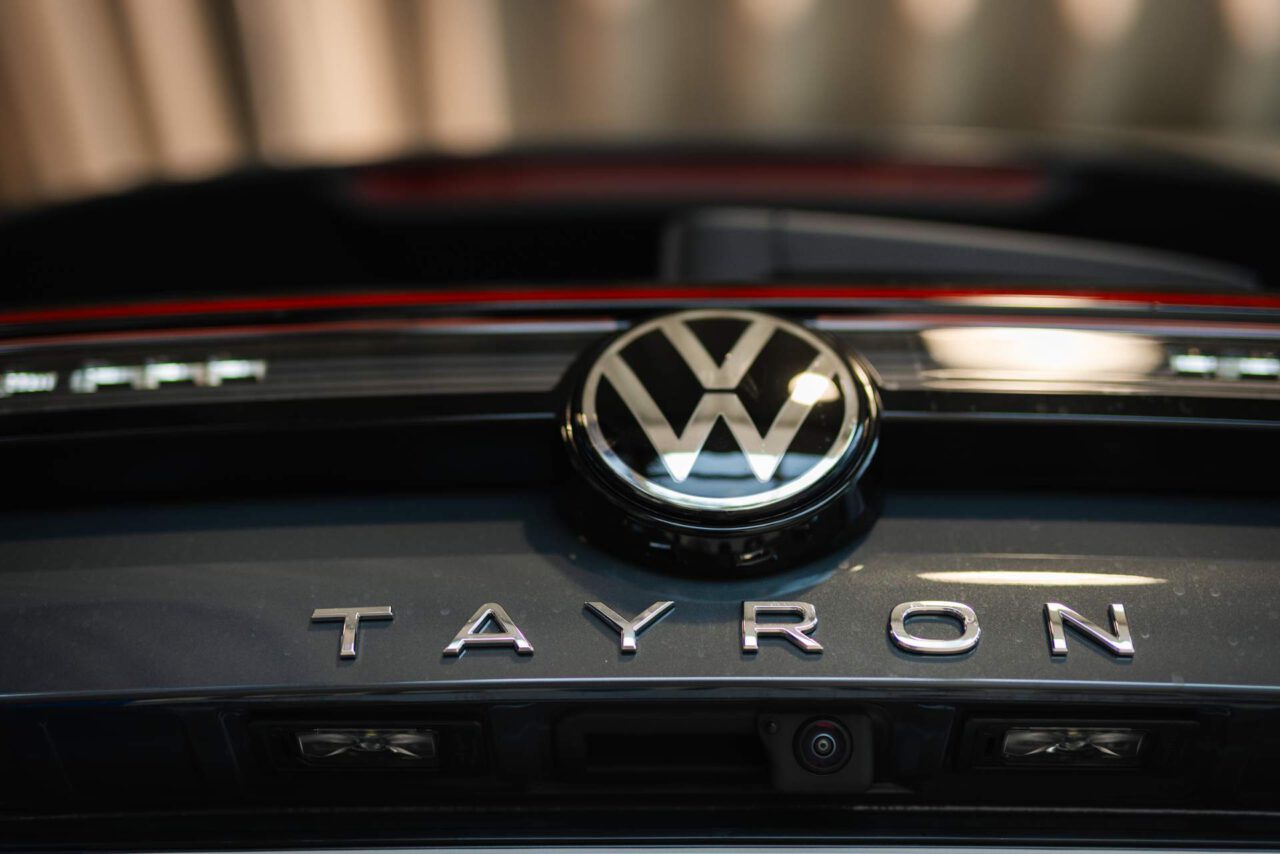 Nahaufnahme des VW-Logos und des Schriftzugs 'TAYRON' auf der Heckklappe eines Fahrzeugs