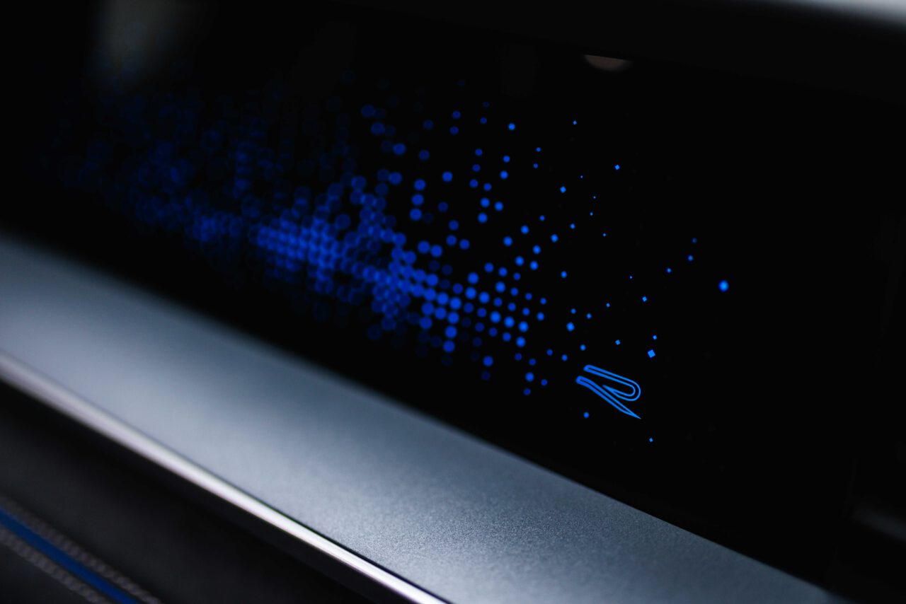 Blaue, punktförmige Lichtmuster auf schwarzem Hintergrund mit kleinem, stilisiertem Buchstaben R in der Ecke