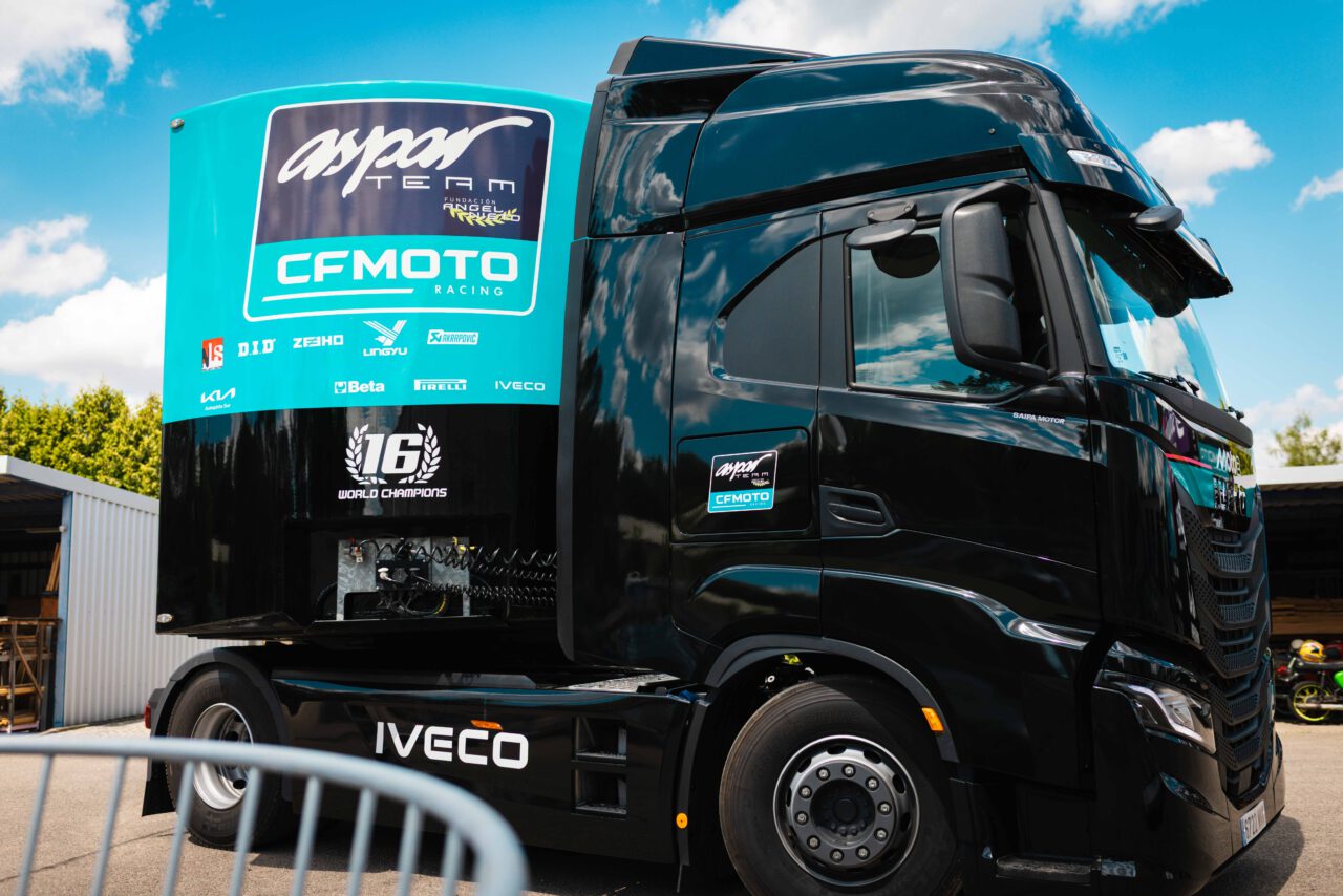 Schwarzer Iveco-Lkw mit Aufschrift 'asper TEAM' und 'CFMOTO RACING' auf der Fahrerkabine, geparkt bei sonnigem Himmel.