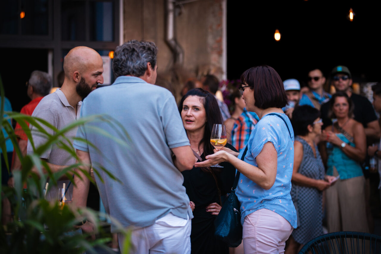 Personengruppe im Gespräch während eines Get-togethers bei einem Firmenevent vor einer rustikalen Industrie-Kulisse.
