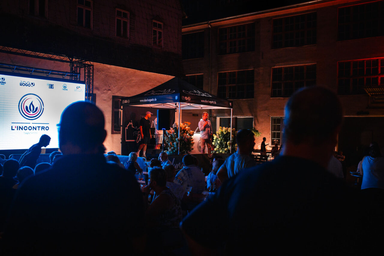 Outdoor-Event mit LED-Screen, Bühnenshow und Zuschauern in einer beleuchteten Industrie-Location bei Dunkelheit.