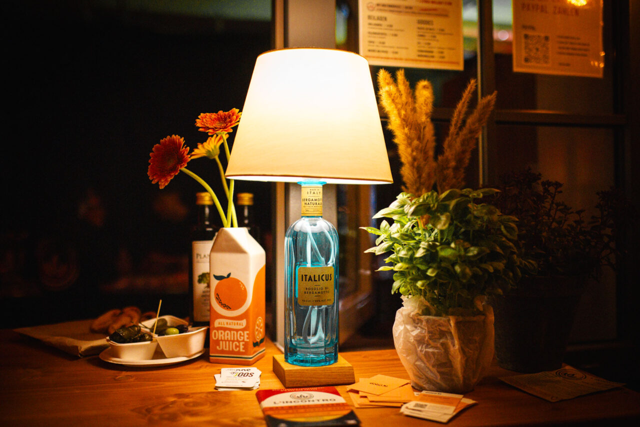 Detailansicht einer Bar-Dekoration mit Vintage-Lampe, Blumen und Basilikum bei einem Event in stimmungsvollem Licht.