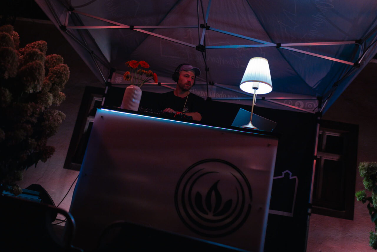 DJ bei einer Abendveranstaltung im Freien unter einem Pavillon mit professioneller Lichttechnik und Branding-Elementen.